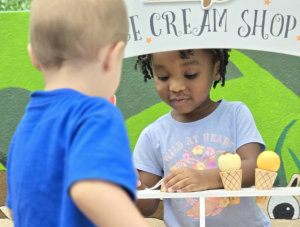 a young girl, standing behind a toy ice cream shop play set